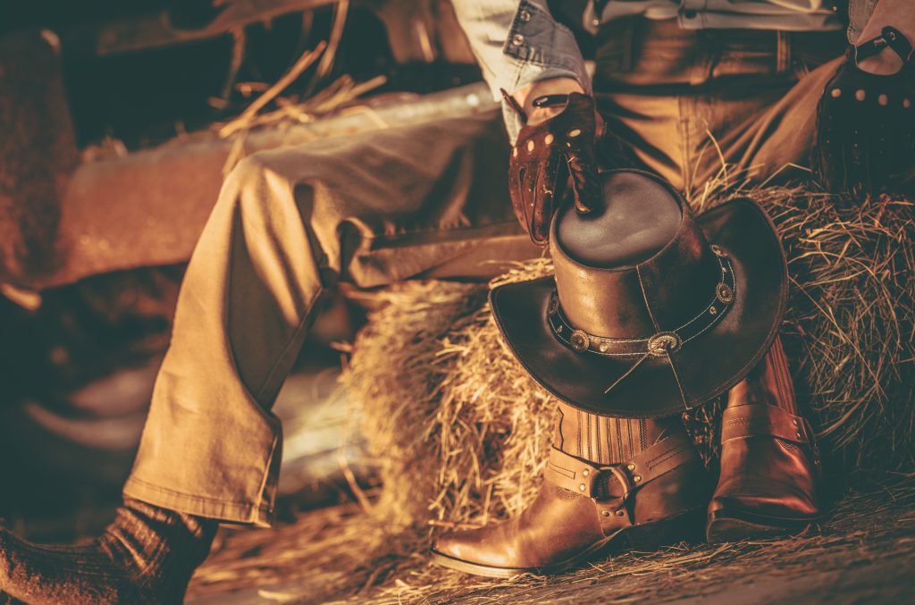 Caucasian Western Wearing American Cowboy Taking Rest Inside His Barn. Cowboy Leather Shoes and Hat.